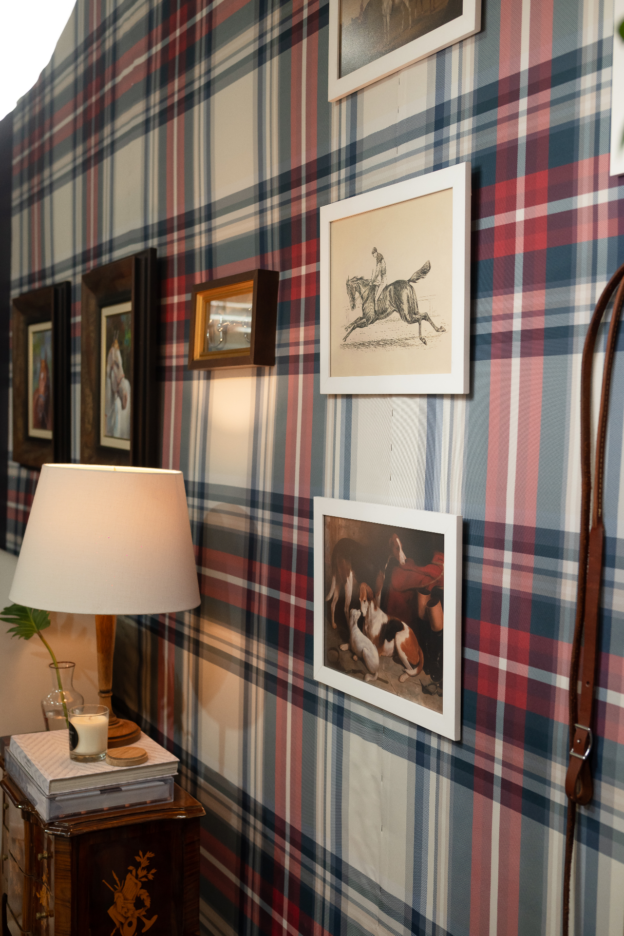Parede revestida em papel tartan com galeria de quadros equestres e abajur clássico