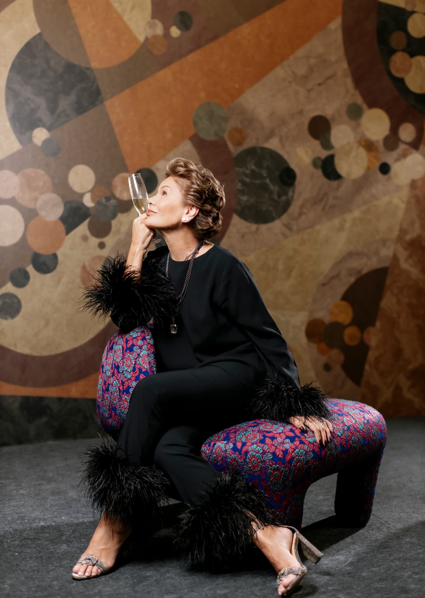 Participante sentada em poltrona estampada diante de painel artístico