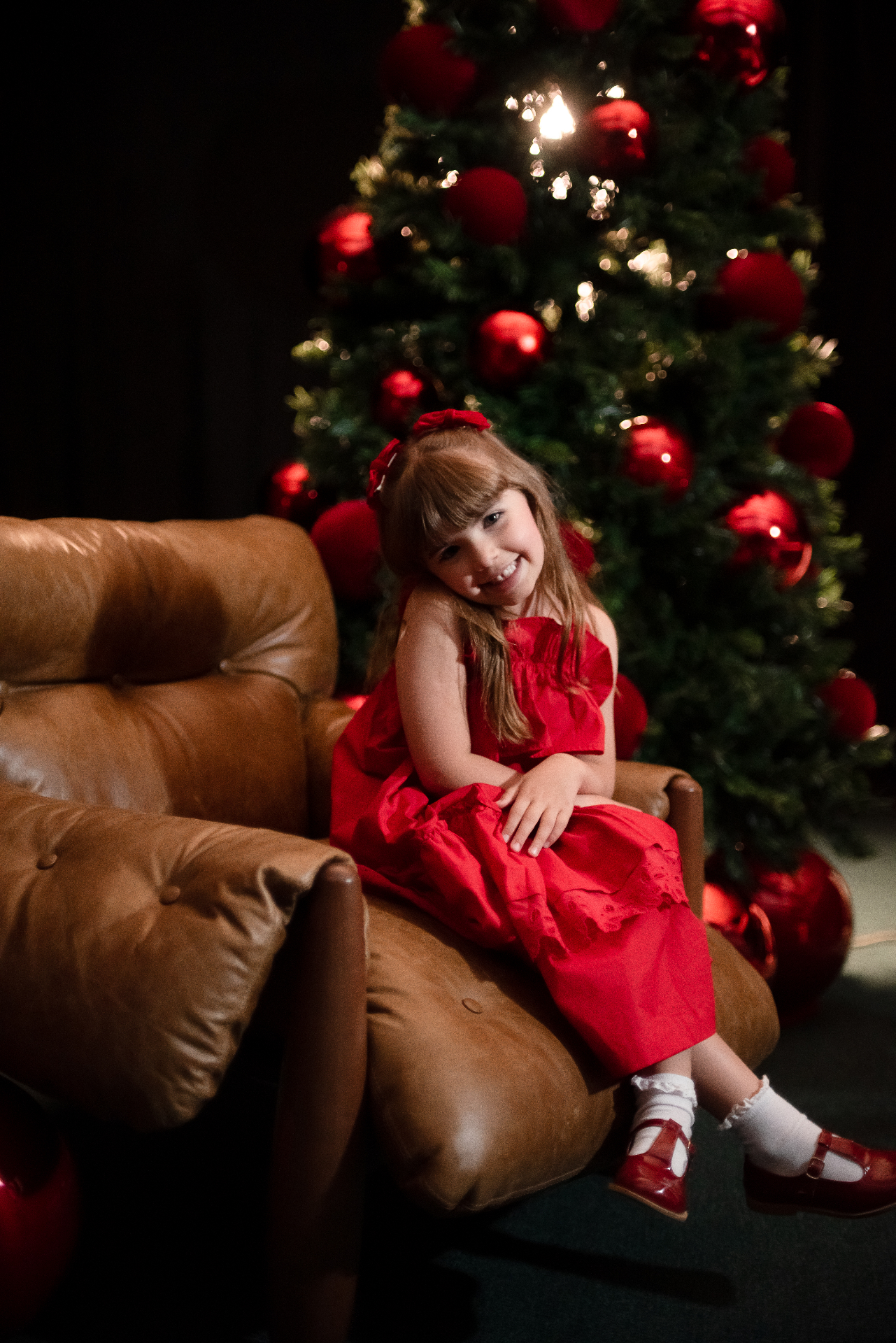 Menina de vestido vermelho na poltrona, junto à árvore de Natal