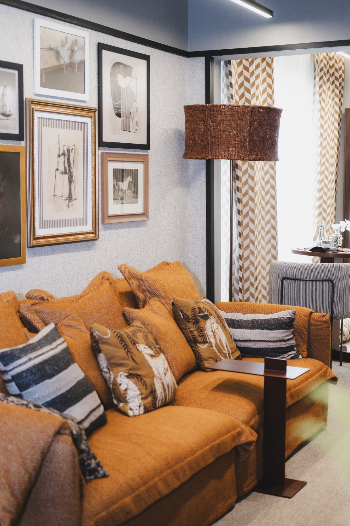 Sala com sofá terracota, parede de quadros e cortina cheurom dourado no ambiente Cosmopolitan