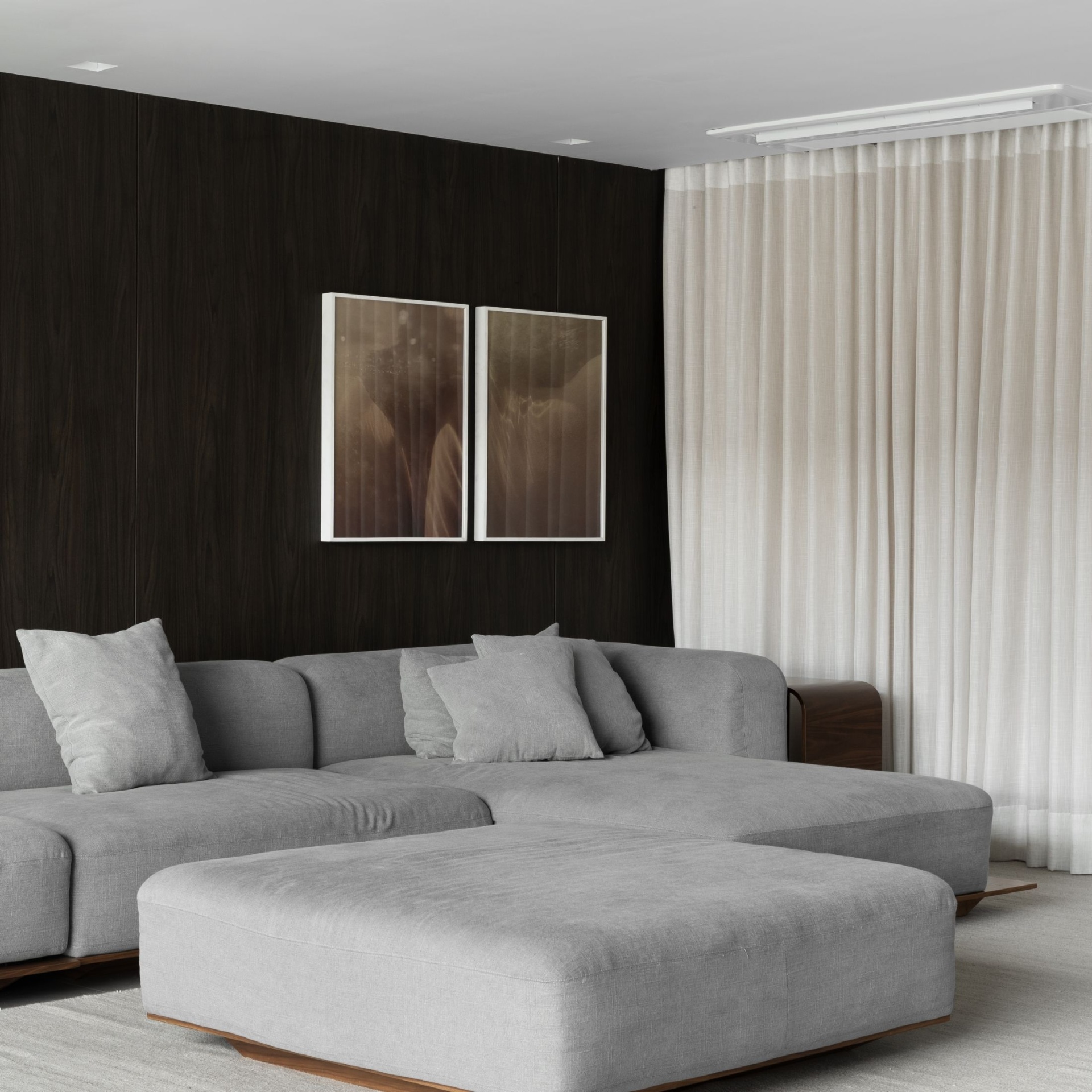 Sofá Platô ambientado em sala com chaise e pufe, painel de madeira e cortinas de linho