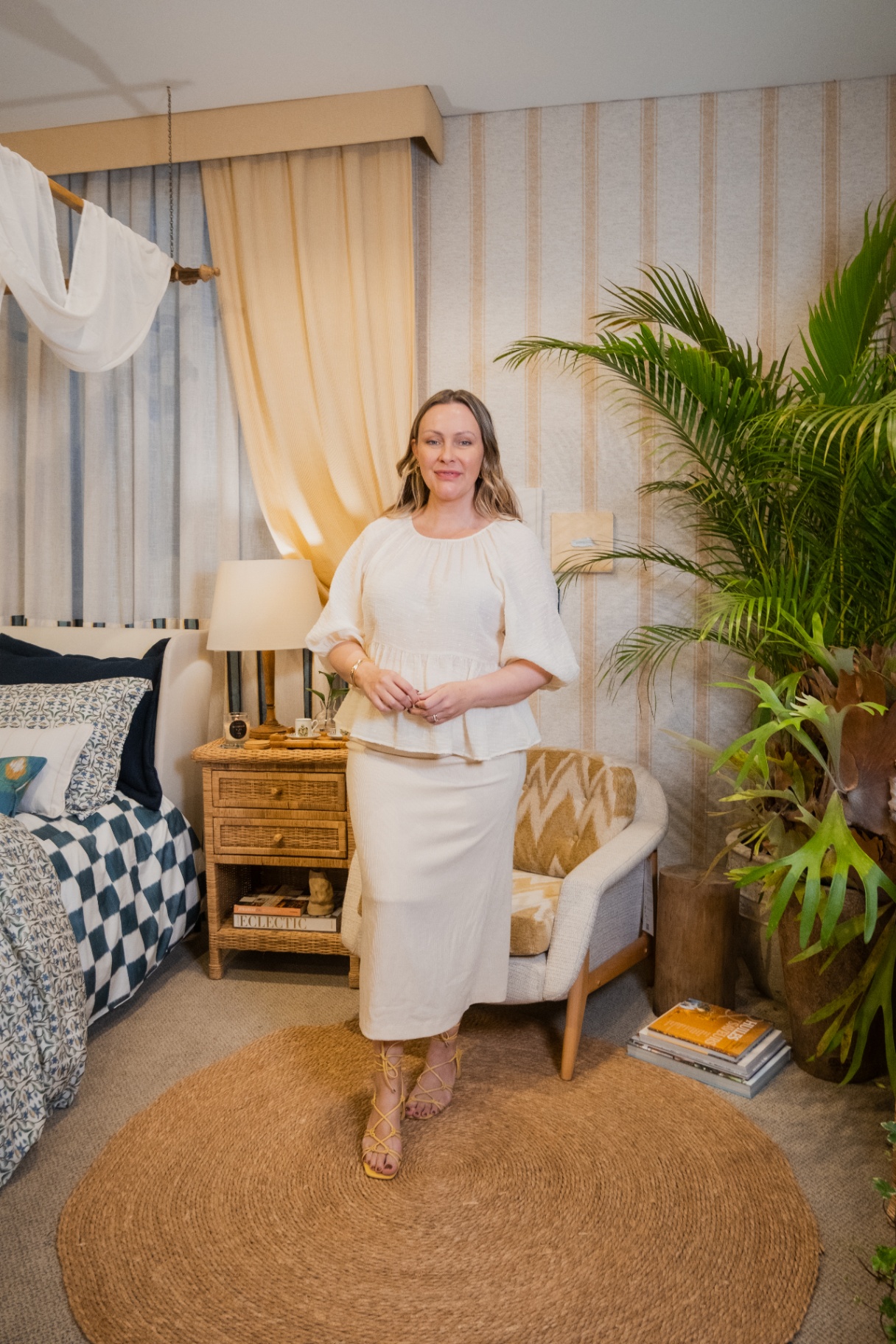 Retrato no ambiente Entreposto Zanzibar, com cortinas listradas, poltrona cheurom mostarda e cama com xadrez azul