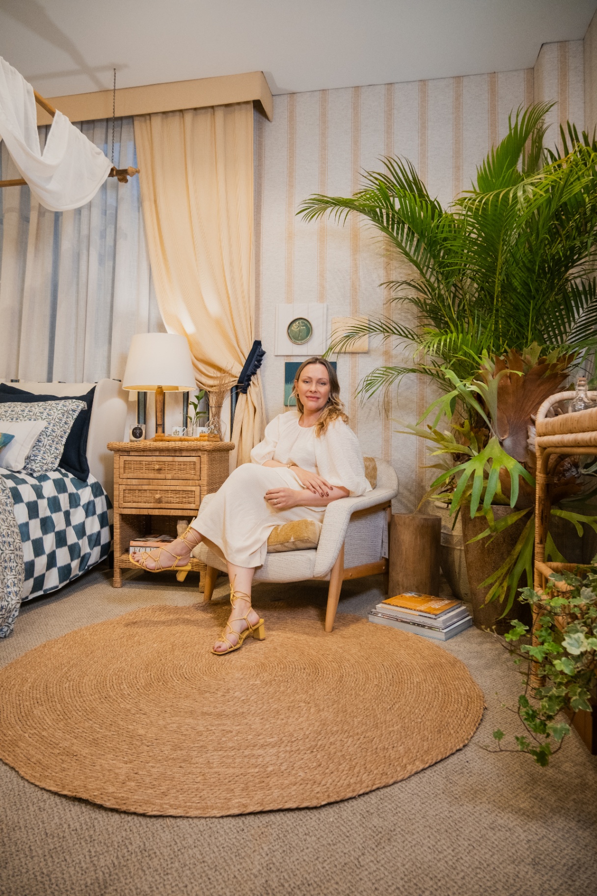 Retrato de Daniela Luize sentada na poltrona cheurom mostarda do ambiente Zanzibar, entre cortinas e plantas