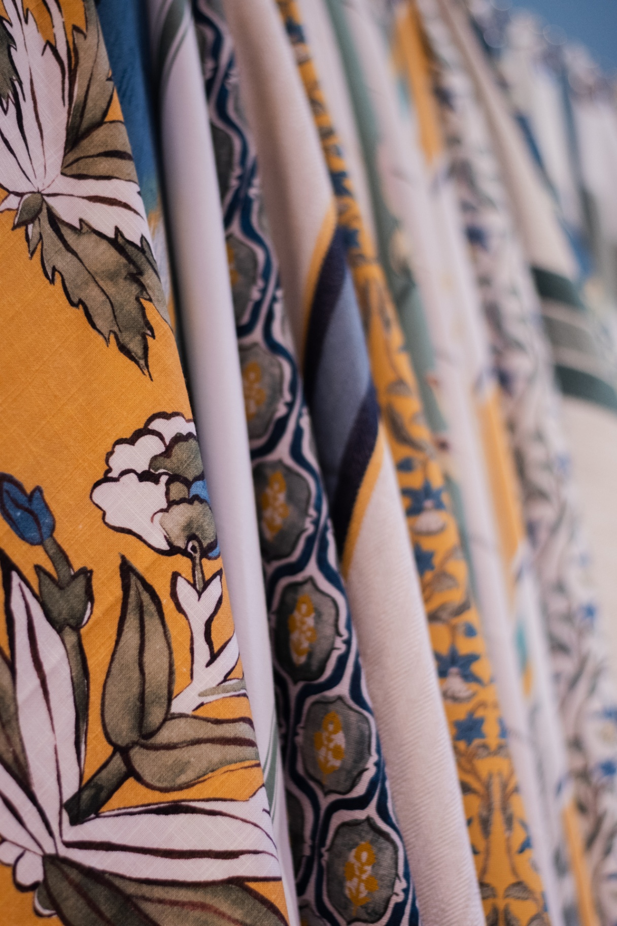 Detalhe de tecidos Entreposto Zanzibar com estampas florais mostarda, listras e florais azuis suspensos