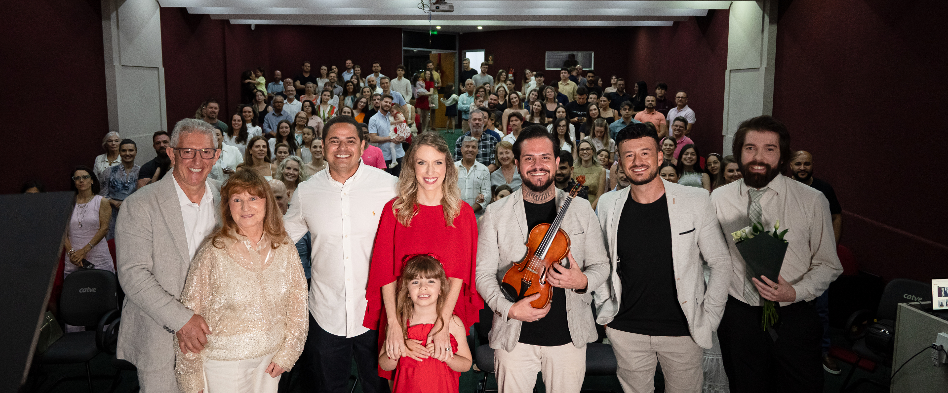 Família e músicos no palco, com o auditório lotado ao fundo