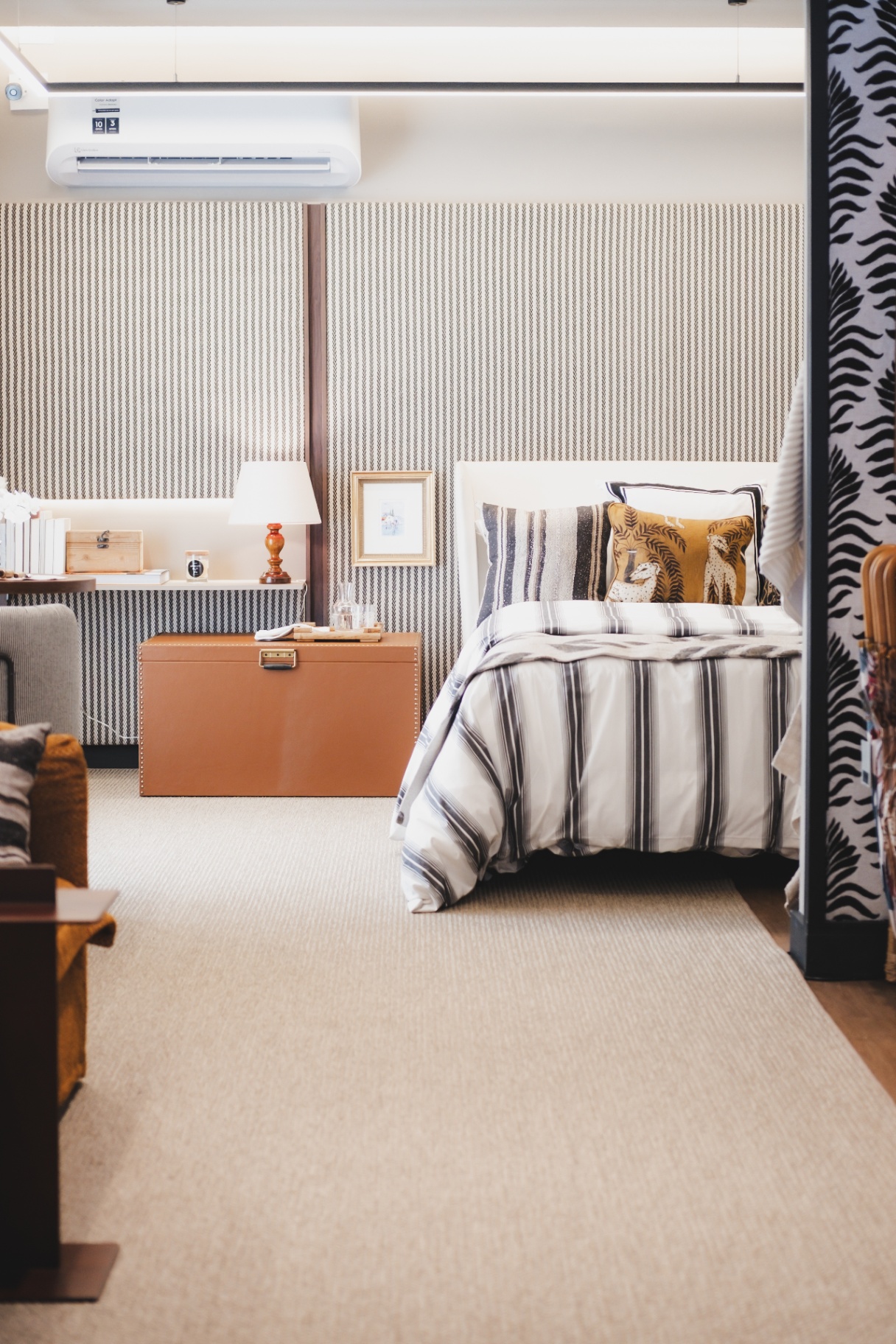 Quarto Cosmopolitan com papel de parede cheurom, baú de couro caramelo e roupa de cama listrada