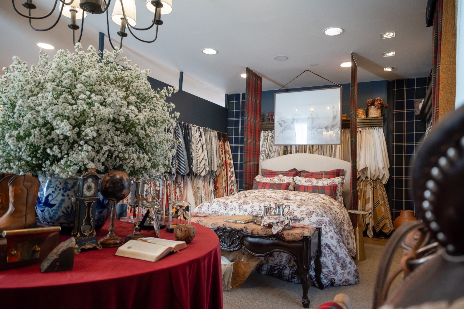 Vista ampla do ambiente Tartans, com cama paisley, cortinas xadrez e arranjo de flores brancas