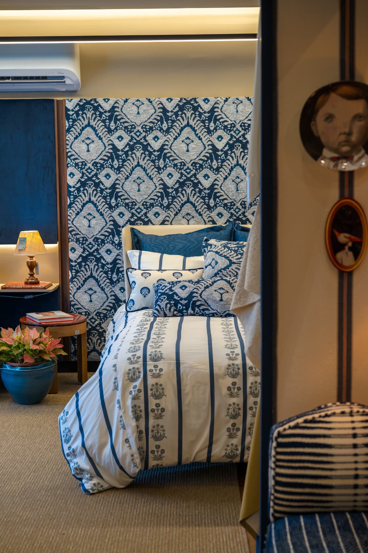 Quarto da Coleção Comporta, da Entreposto, com cabeceira de jacquard azul, cama de listras e retratos em molduras ovais