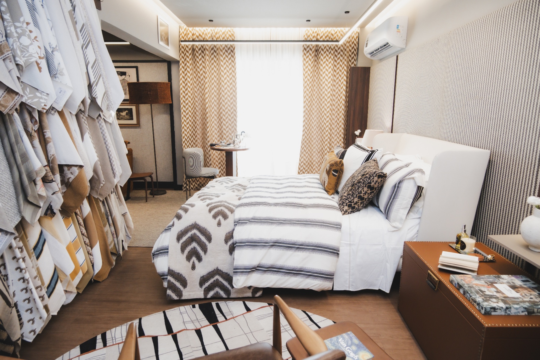 Quarto Cosmopolitan com cama de roupa de cama listrada, cortinas cheurom dourado e arara de tecidos Entreposto