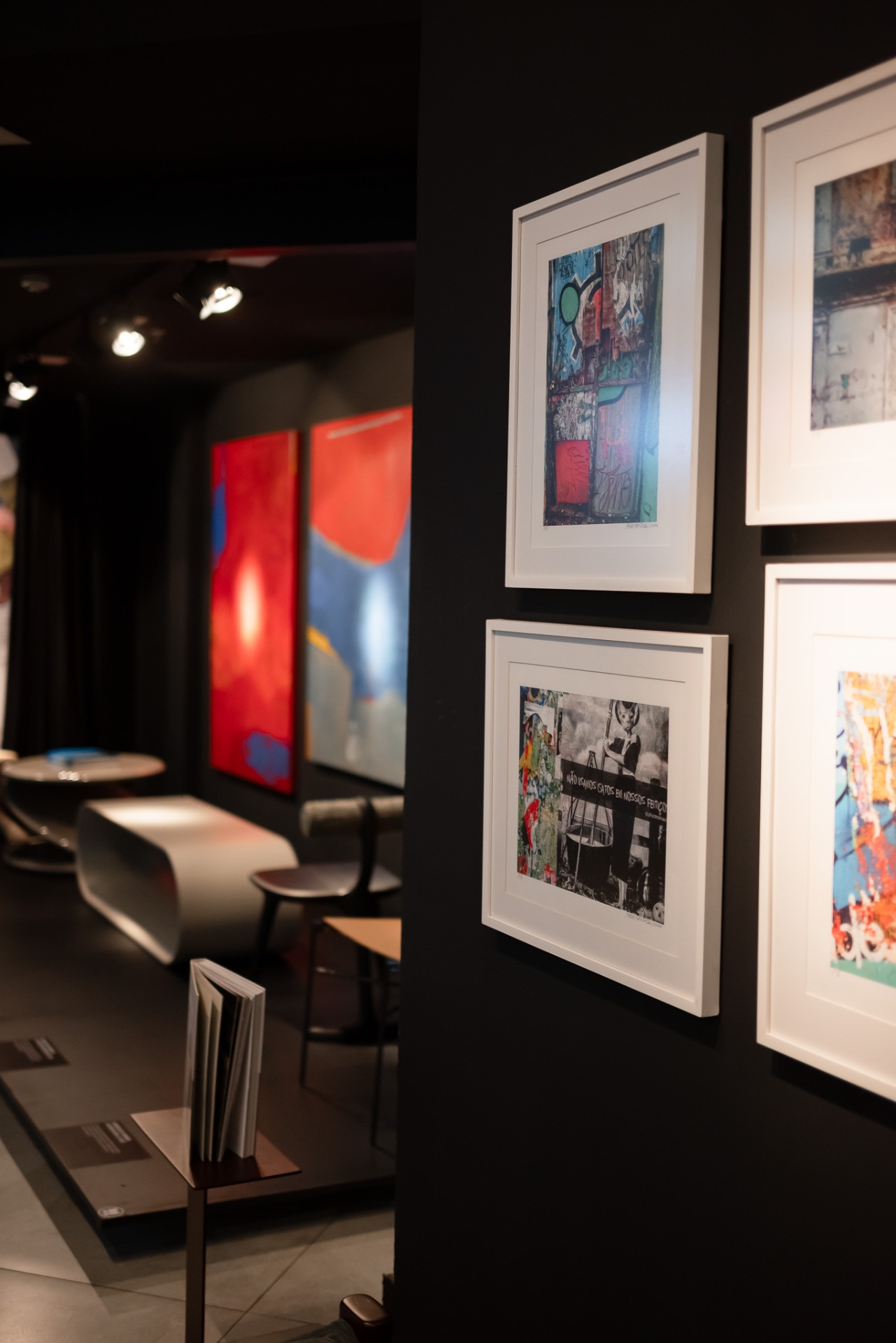 Parede com fotografias emolduradas em diálogo com pinturas contemporâneas