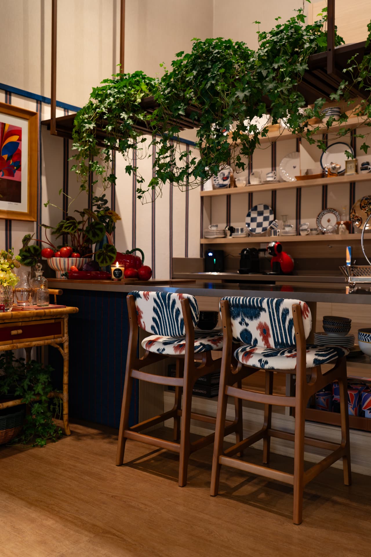 Banquetas de madeira estofadas com tecido ikat azul e vermelho junto ao balcão da cozinha, com heras suspensas