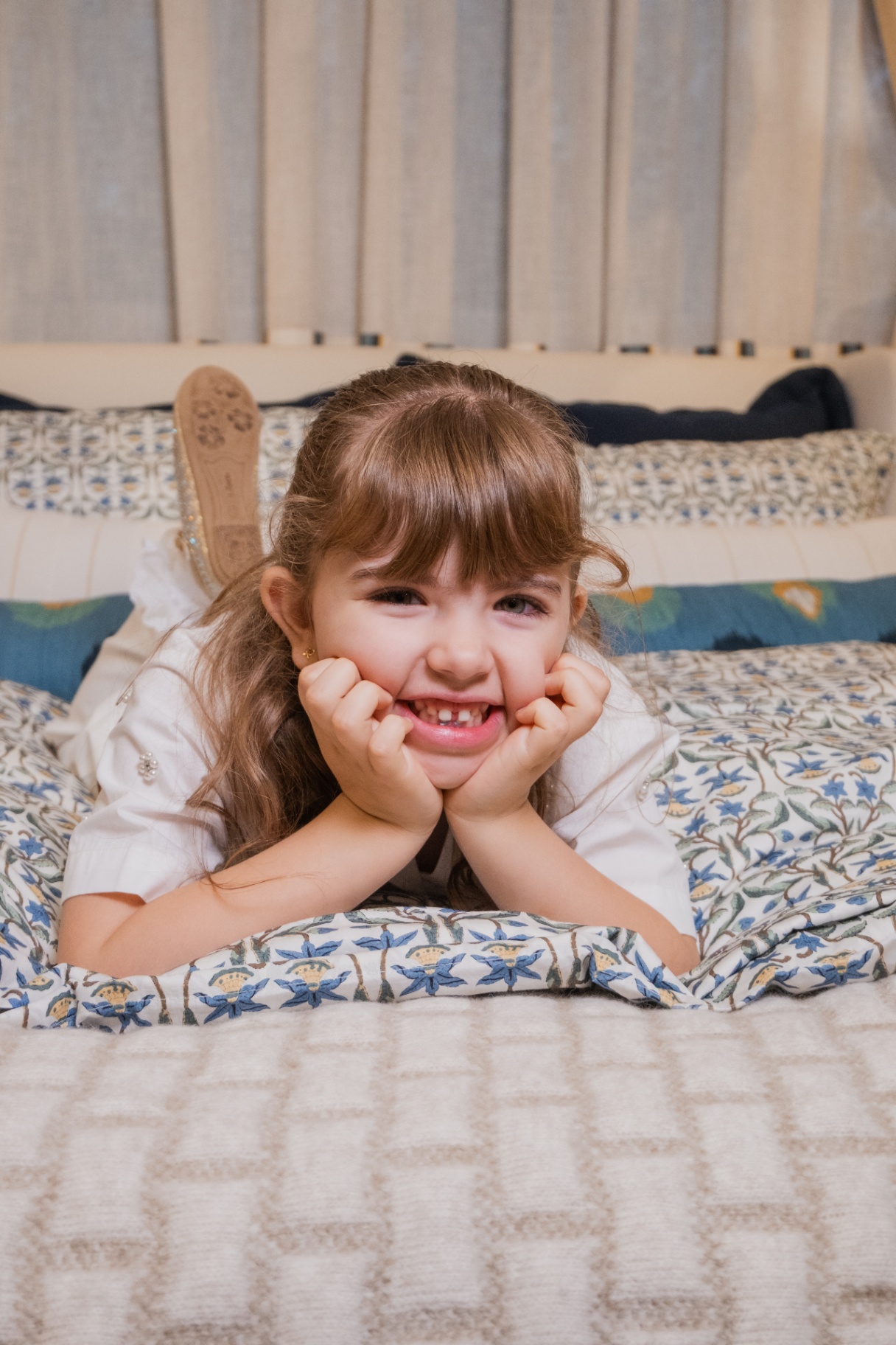 Menina sorrindo sobre a cama com roupa de cama floral azul Entreposto no ambiente Zanzibar